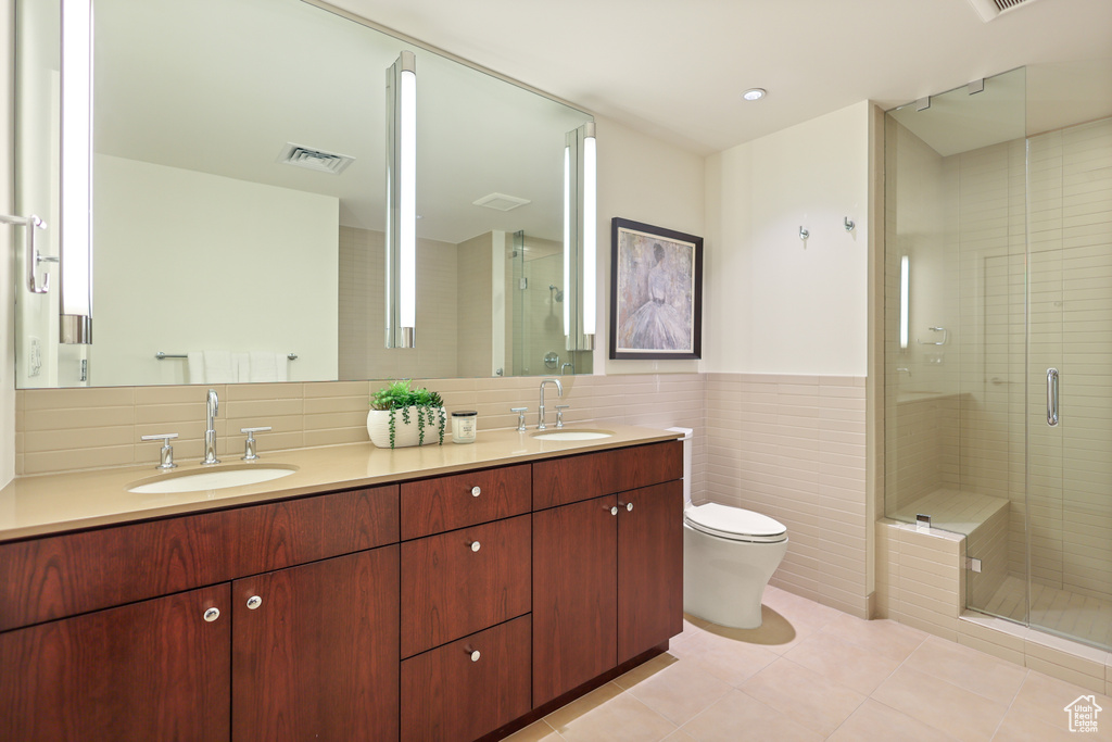 Full bathroom with tile walls, a stall shower, double vanity, toilet, and tile patterned floors