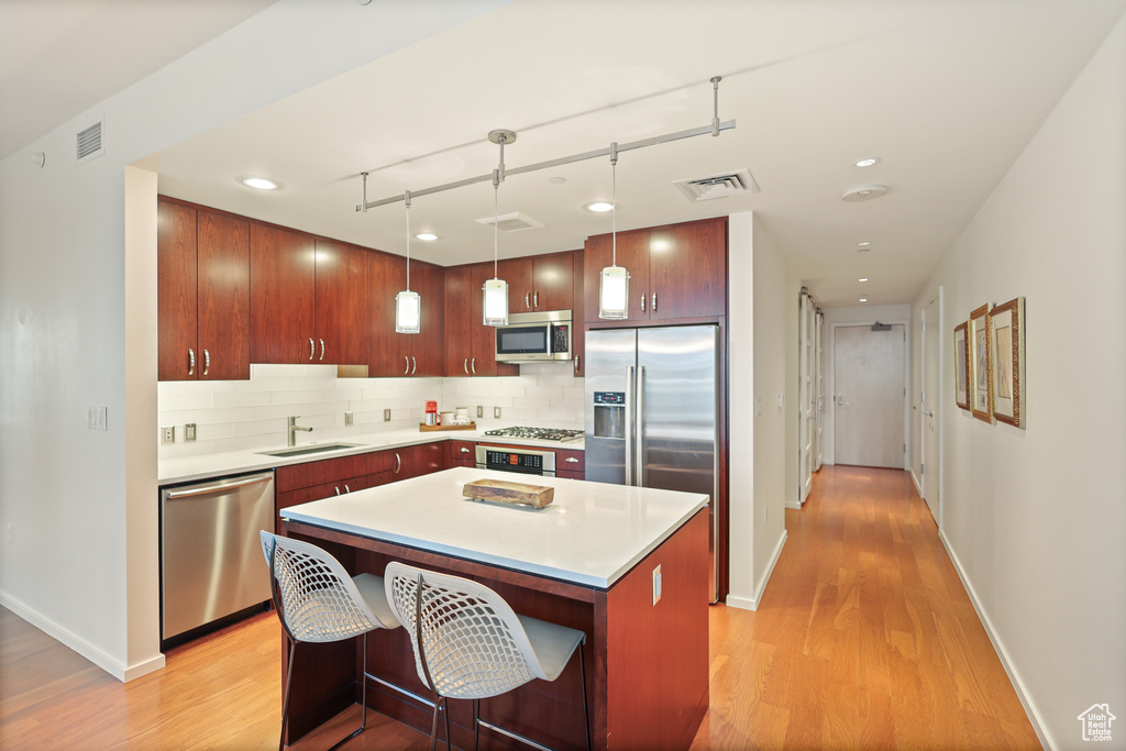 Kitchen with stainless steel appliances, light wood-type flooring, decorative backsplash, light countertops, and recessed lighting