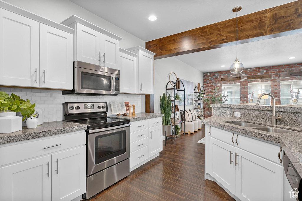 Kitchen featuring stainless steel appliances, a sink, backsplash, beamed ceiling, and white cabinets