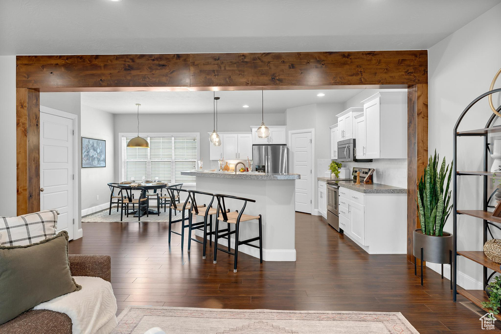 Kitchen featuring appliances with stainless steel finishes, a kitchen bar, dark wood-style floors, an island with sink, and white cabinetry