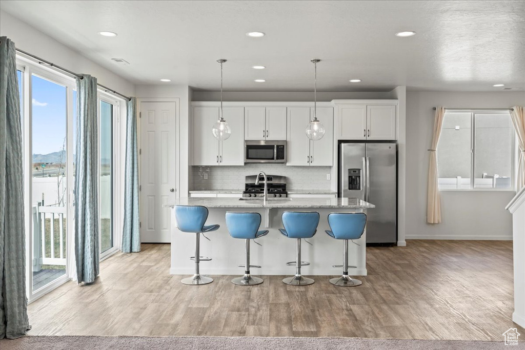 Kitchen with appliances with stainless steel finishes, a sink, a kitchen island with sink, tasteful backsplash, and a kitchen breakfast bar