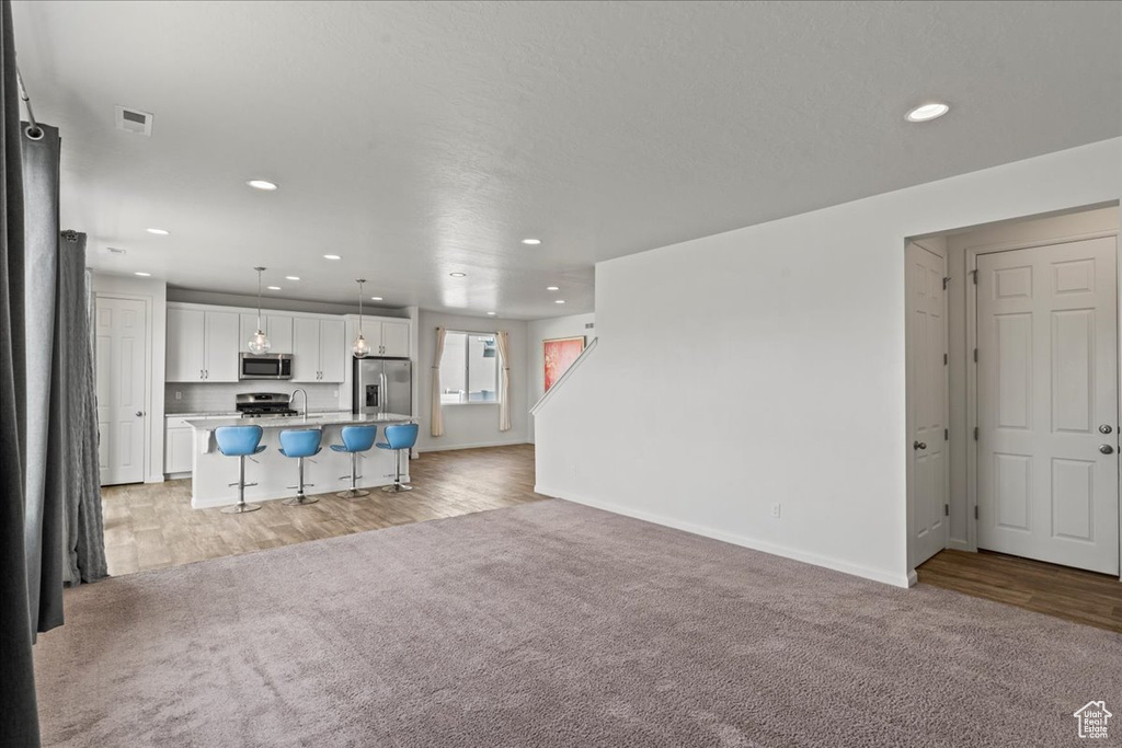 Unfurnished living room featuring recessed lighting, light carpet, baseboards, light wood-type flooring, and a sink