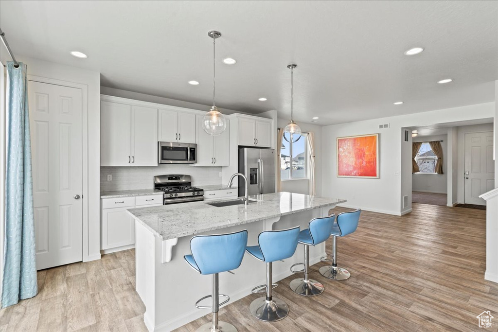 Kitchen with appliances with stainless steel finishes, a sink, light wood finished floors, a kitchen island with sink, and recessed lighting