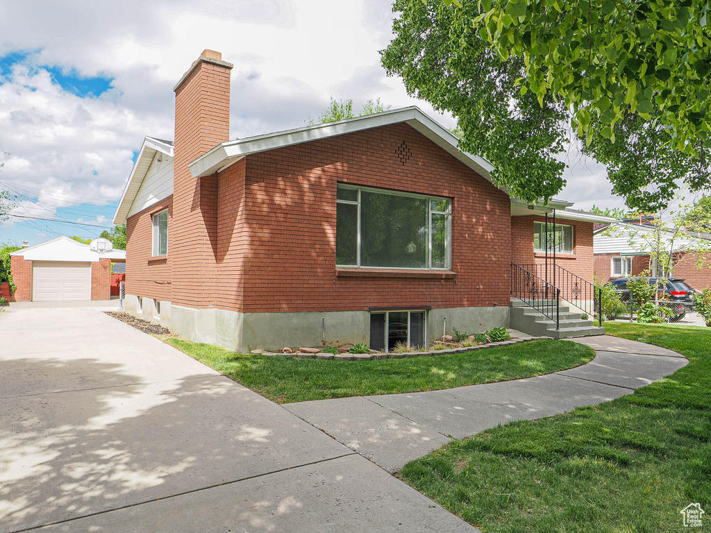 View of property exterior with a chimney, an outdoor structure, concrete driveway, a yard, and brick siding