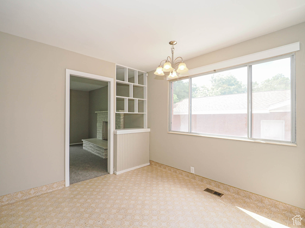 Carpeted spare room featuring a chandelier and a fireplace with raised hearth