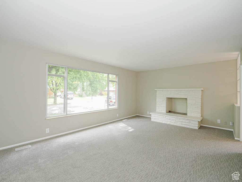 Unfurnished living room featuring carpet flooring, baseboards, and a brick fireplace