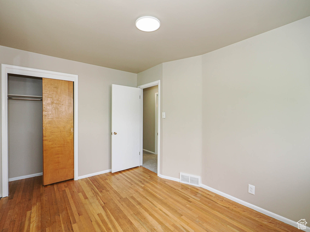 Unfurnished bedroom with light wood-style floors, baseboards, and a closet