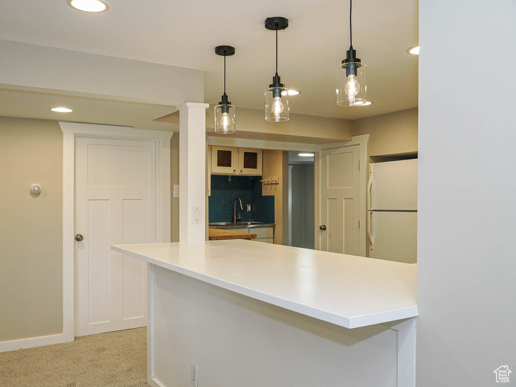 Kitchen with freestanding refrigerator, a sink, a peninsula, recessed lighting, and hanging light fixtures