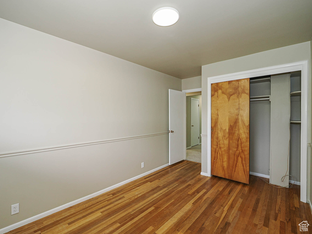 Unfurnished bedroom featuring wood finished floors, a closet, and baseboards