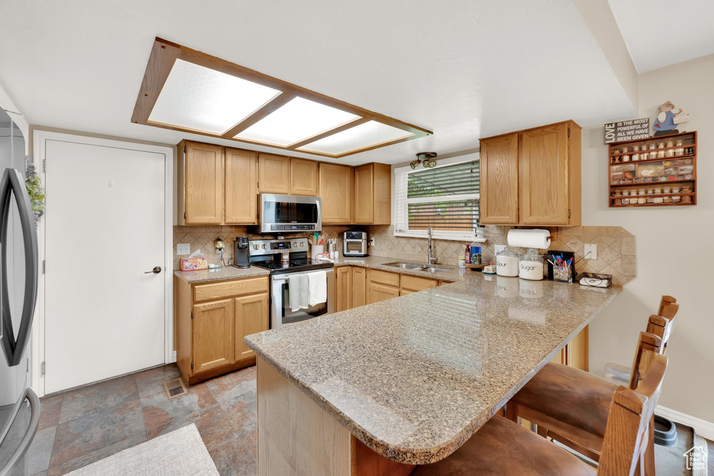 Kitchen featuring appliances with stainless steel finishes, a sink, a peninsula, decorative backsplash, and a breakfast bar