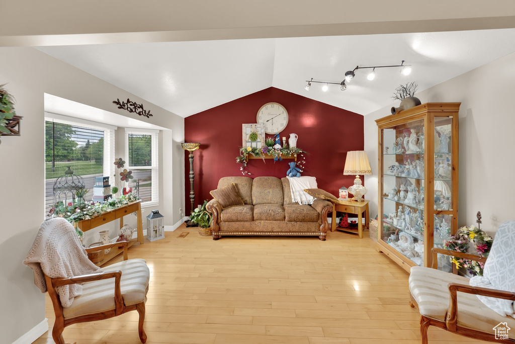 Living room featuring lofted ceiling, wood finished floors, rail lighting, and baseboards