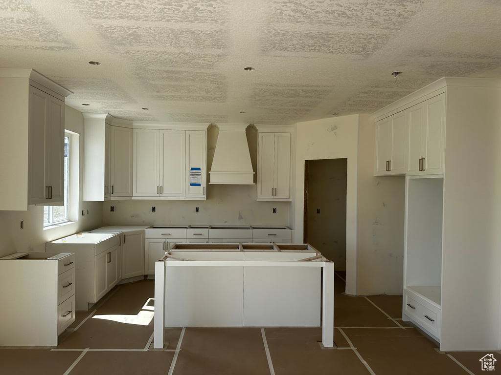 Kitchen featuring custom exhaust hood, a kitchen island, a textured ceiling, and white cabinetry