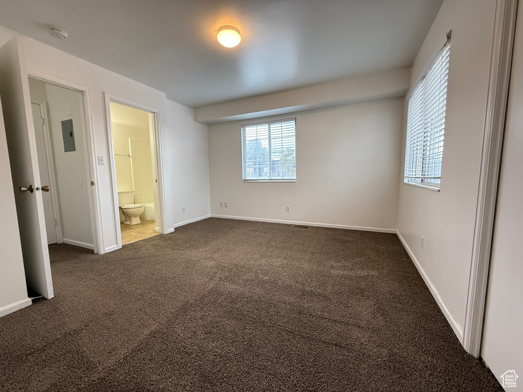 Unfurnished bedroom featuring dark carpet, multiple windows, baseboards, and connected bathroom