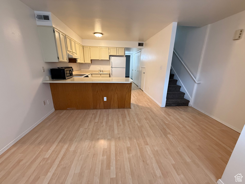 Kitchen with freestanding refrigerator, a peninsula, under cabinet range hood, and light wood-type flooring