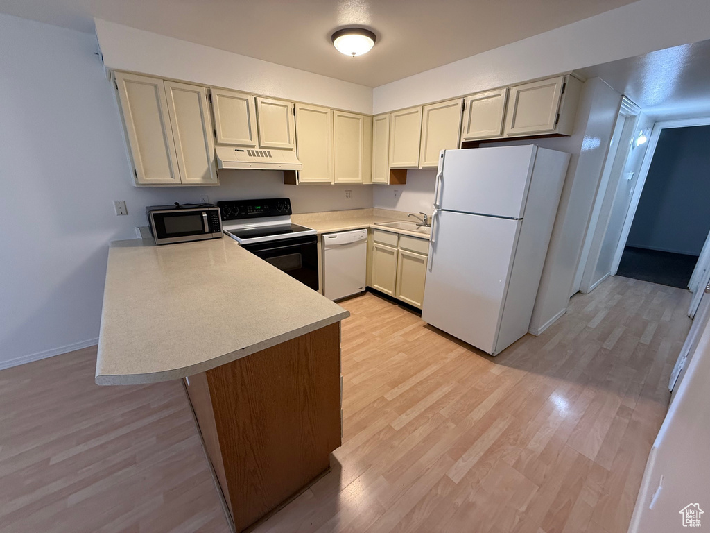 Kitchen with white appliances, under cabinet range hood, a sink, a peninsula, and light countertops