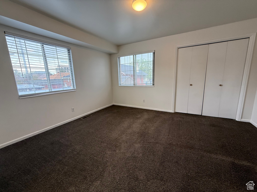 Unfurnished bedroom with dark carpet, baseboards, and a closet