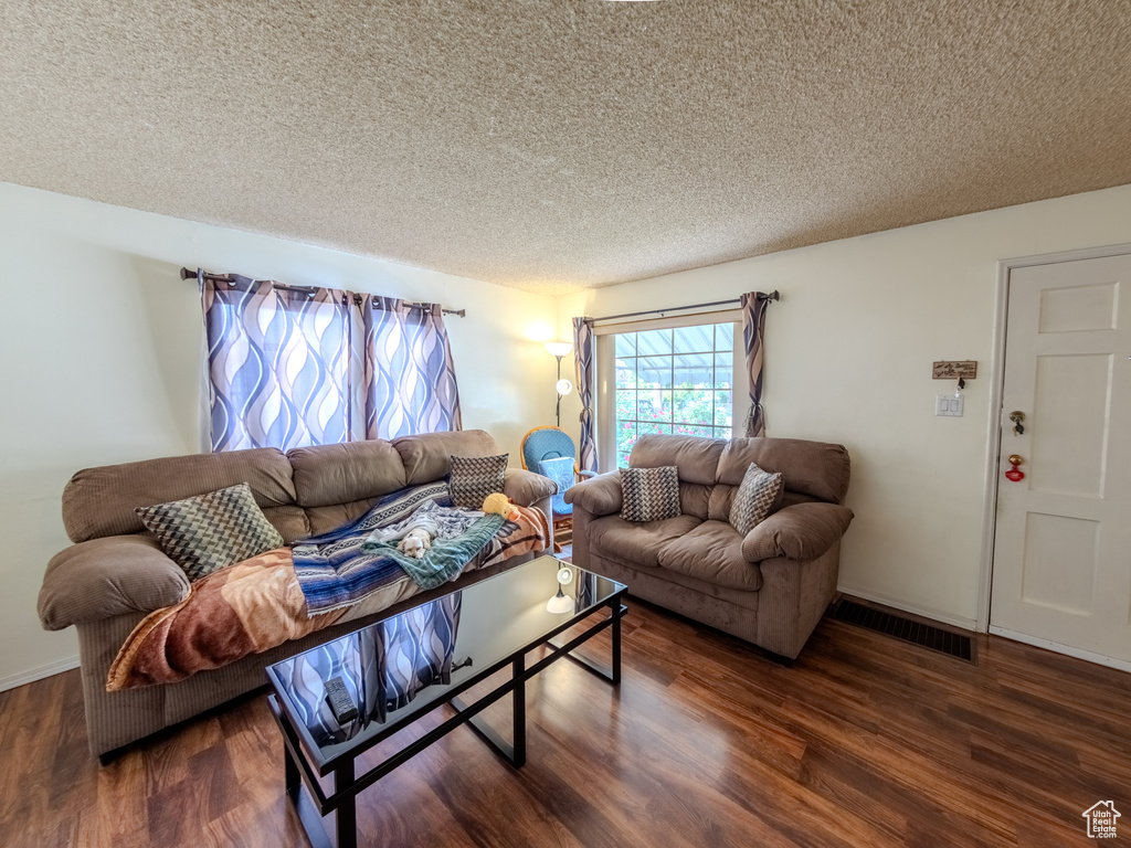 Living area featuring dark wood-type flooring, a textured ceiling, and baseboards