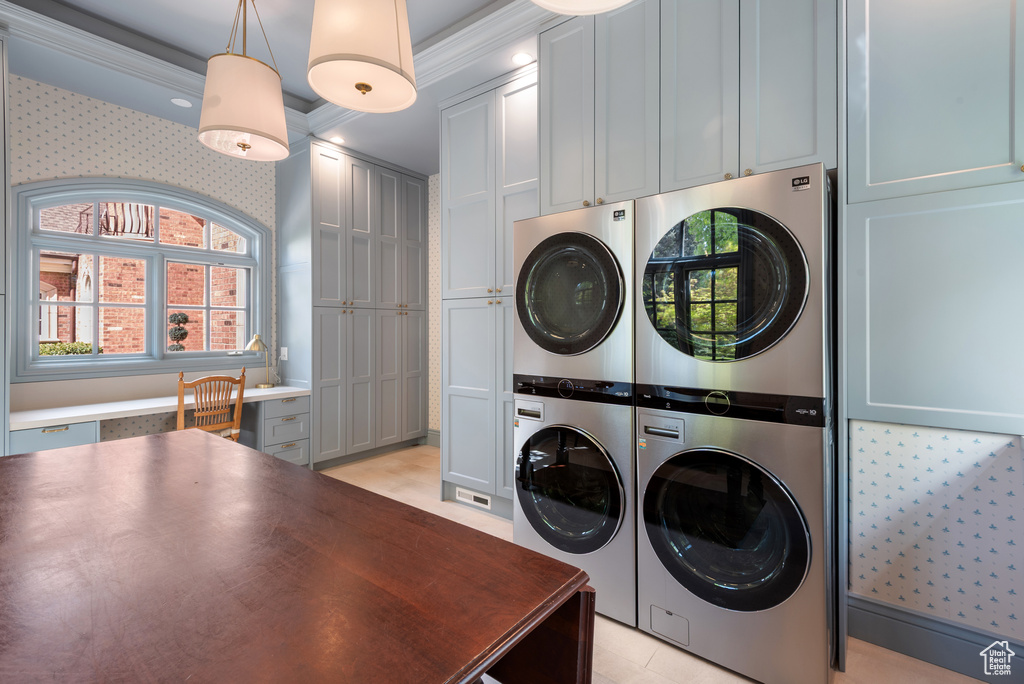 Clothes washing area featuring estacked washer and dryer, cabinet space, and crown molding
