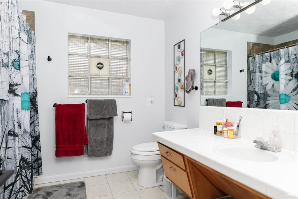 Full bath with toilet, tile patterned floors, vanity, a shower with curtain, and baseboards