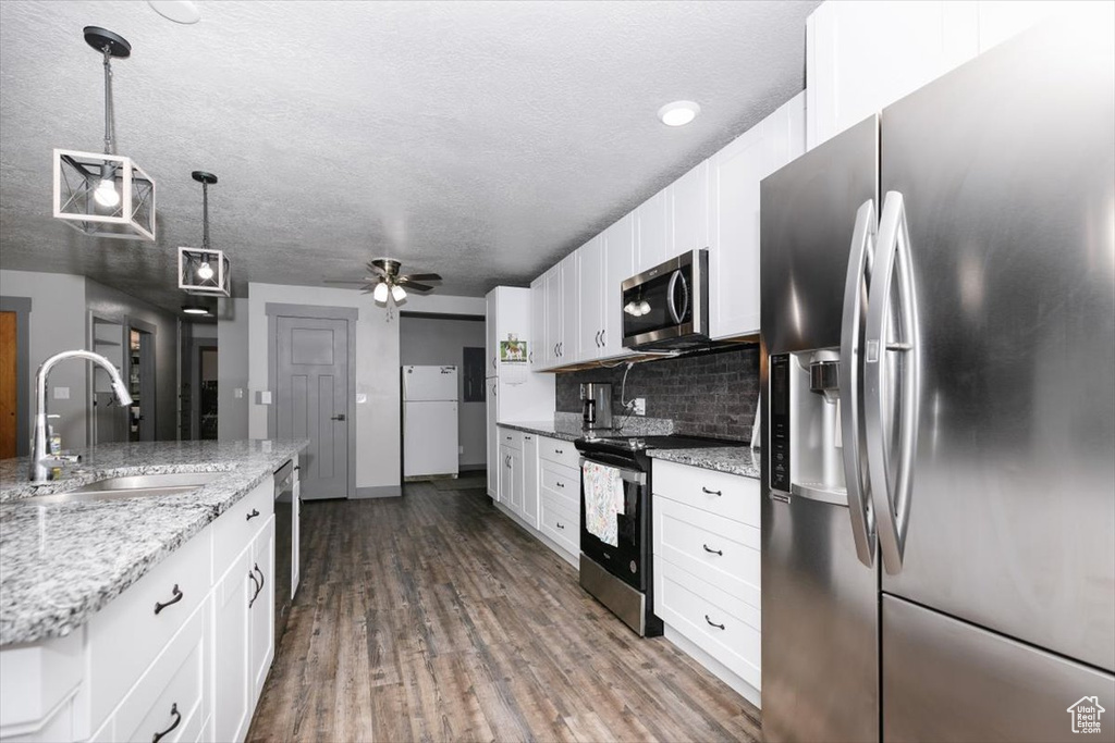 Kitchen with appliances with stainless steel finishes, a sink, white cabinetry, backsplash, and dark wood finished floors