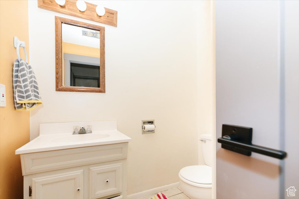 Half bath with vanity, toilet, tile patterned flooring, and baseboards