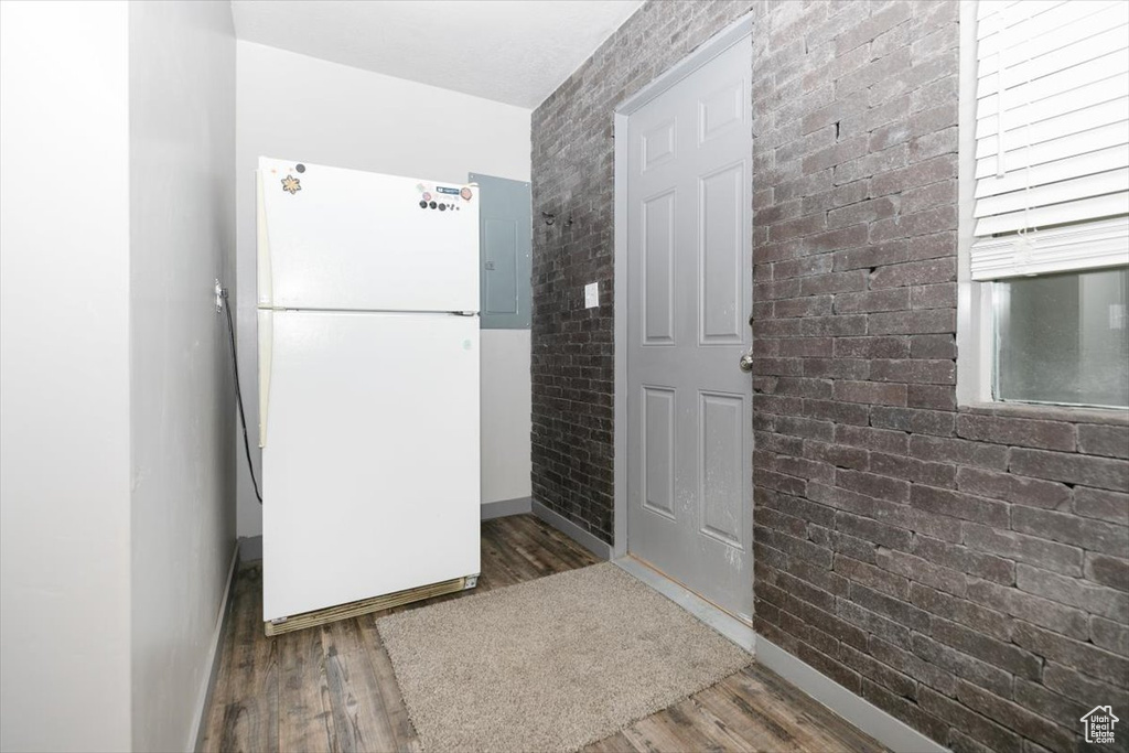 Kitchen with freestanding refrigerator, baseboards, wood finished floors, brick wall, and electric panel
