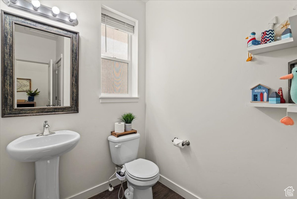 Half bathroom with baseboards, toilet, and wood finished floors