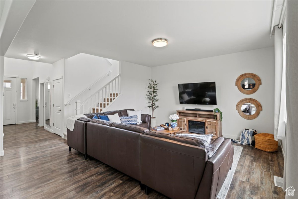 Living room with dark wood-style flooring, stairs, and baseboards