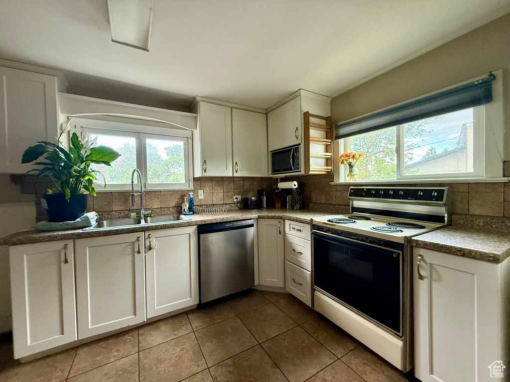 Kitchen featuring stainless steel appliances, a sink, tasteful backsplash, light tile patterned floors, and white cabinets