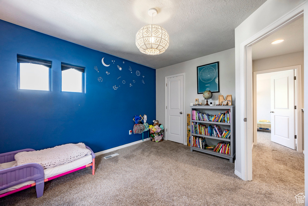 Carpeted bedroom with a chandelier, baseboards, and a textured ceiling