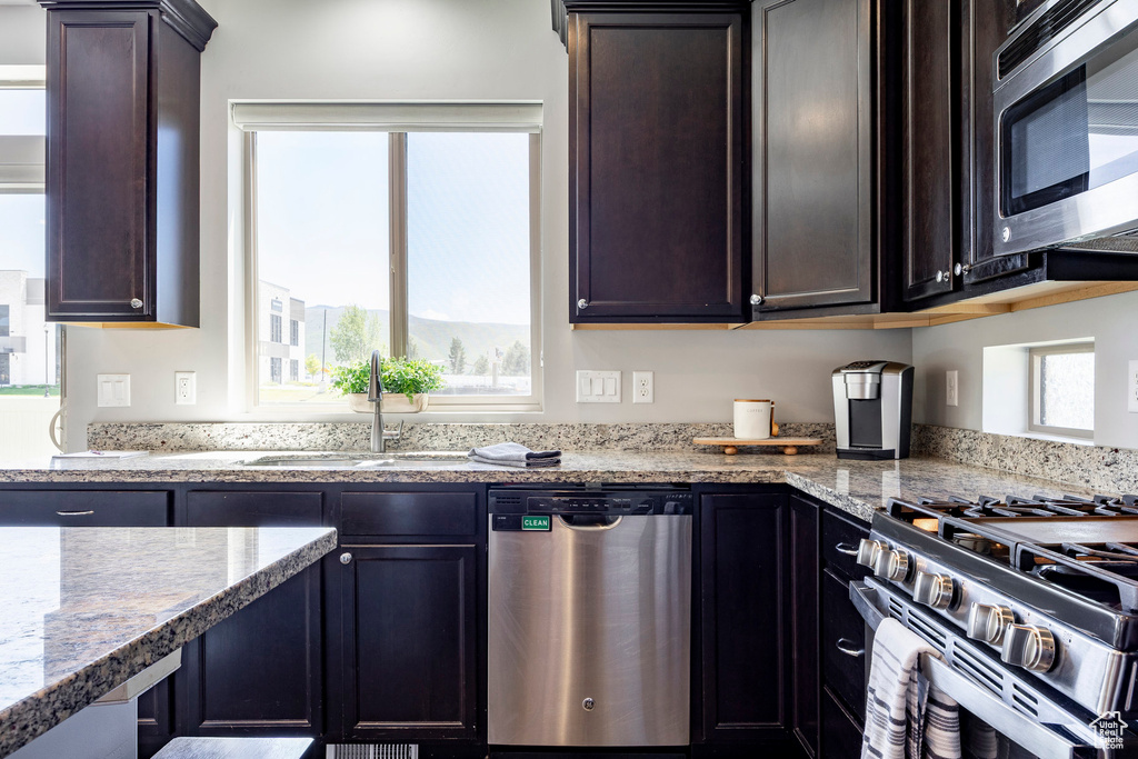 Kitchen featuring stainless steel appliances, a sink, light stone countertops, and dark brown cabinets