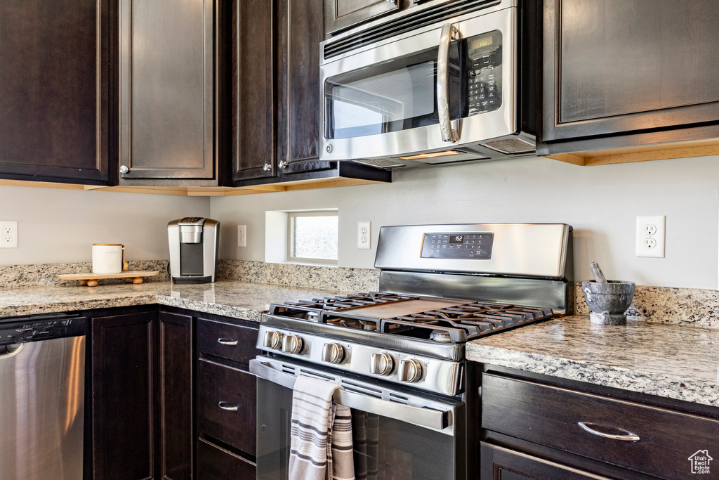 Kitchen with appliances with stainless steel finishes, dark brown cabinetry, and light stone countertops