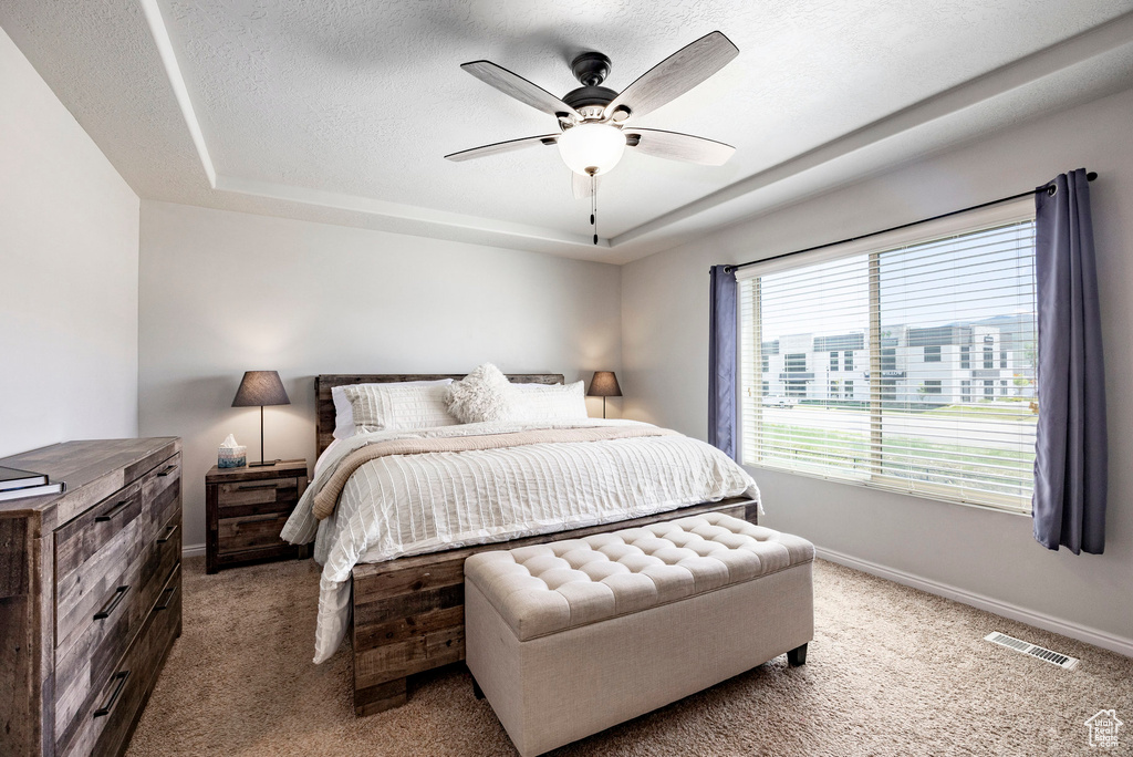 Bedroom with light carpet, a tray ceiling, baseboards, a ceiling fan, and a textured ceiling
