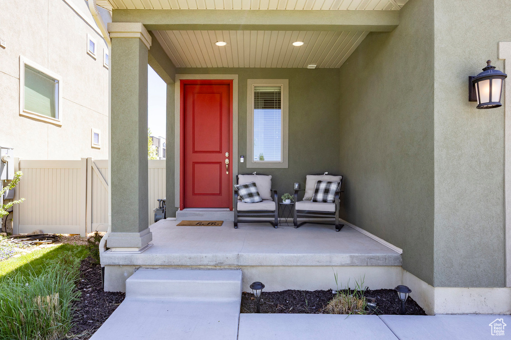 Doorway to property featuring fence, stucco siding, and covered porch