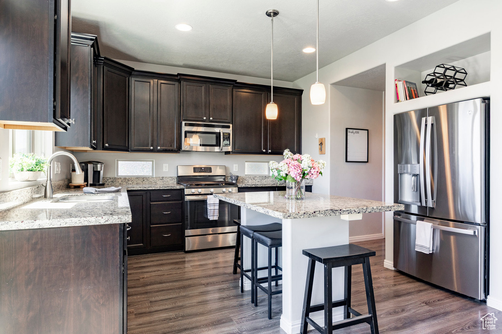 Kitchen with appliances with stainless steel finishes, a sink, dark wood-type flooring, dark brown cabinetry, and a breakfast bar area