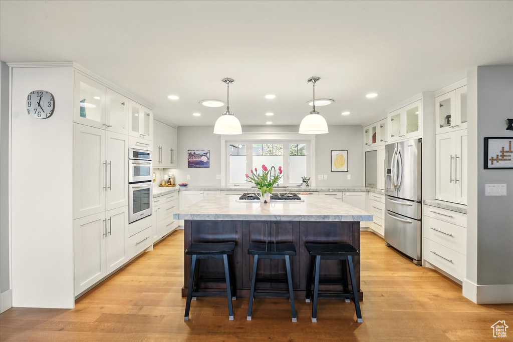 Kitchen with stainless steel appliances, light countertops, a kitchen island, recessed lighting, and a breakfast bar