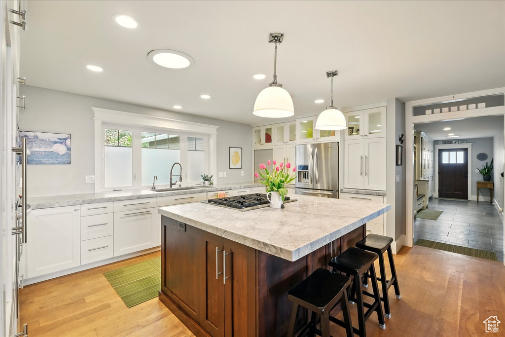 Kitchen with appliances with stainless steel finishes, a sink, a center island, white cabinetry, and a kitchen breakfast bar