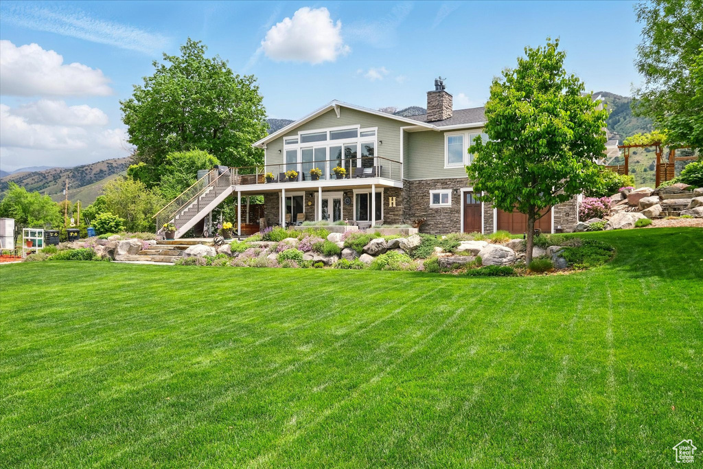 Rear view of property with stone siding, stairs, a deck with mountain view, and a lawn