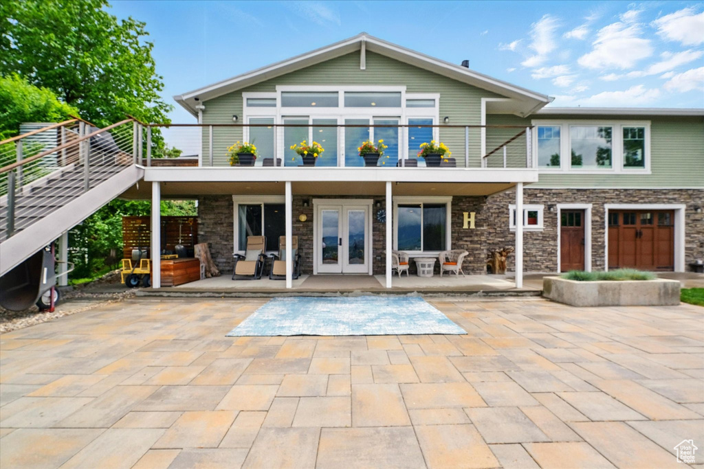 Rear view of property featuring french doors, a balcony, stone siding, and a patio