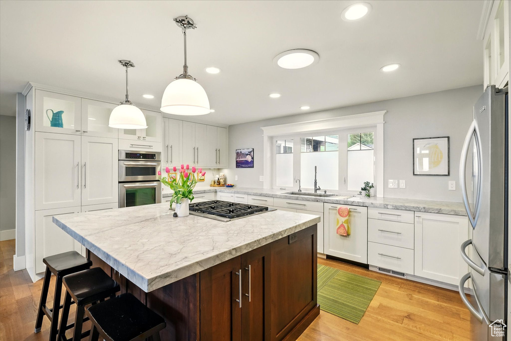 Kitchen with stainless steel appliances, a sink, a kitchen breakfast bar, recessed lighting, and white cabinetry