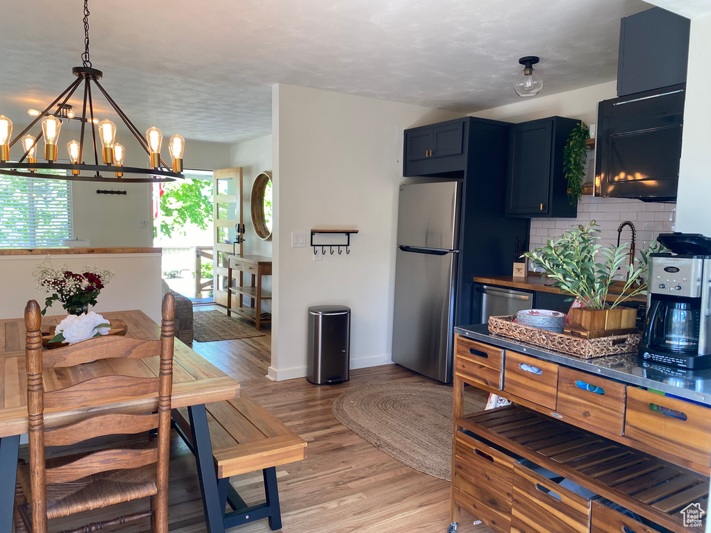 Kitchen featuring stainless steel appliances, a chandelier, blue cabinets, light wood-type flooring, and tasteful backsplash