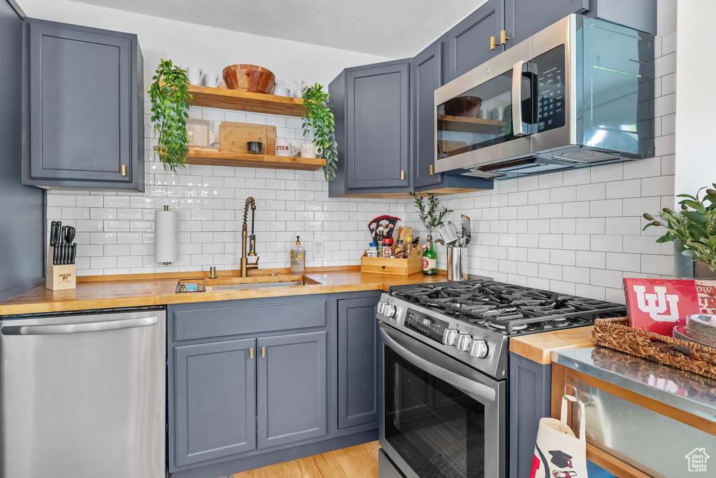 Kitchen featuring stainless steel appliances, a sink, open shelves, wood counters, and backsplash