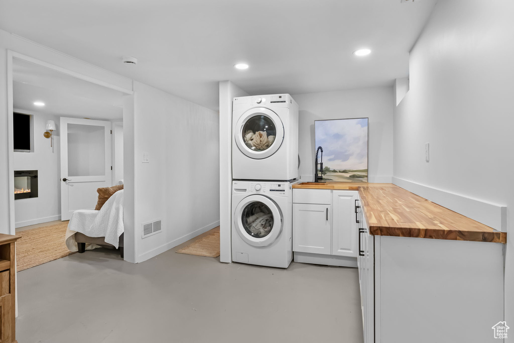 Washroom with stacked washing machine and dryer, cabinet space, a glass covered fireplace, baseboards, and recessed lighting