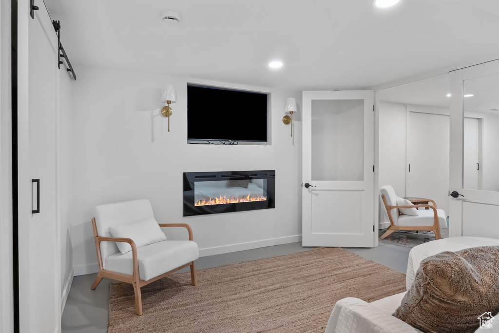Living area featuring a glass covered fireplace, baseboards, recessed lighting, a barn door, and finished concrete floors