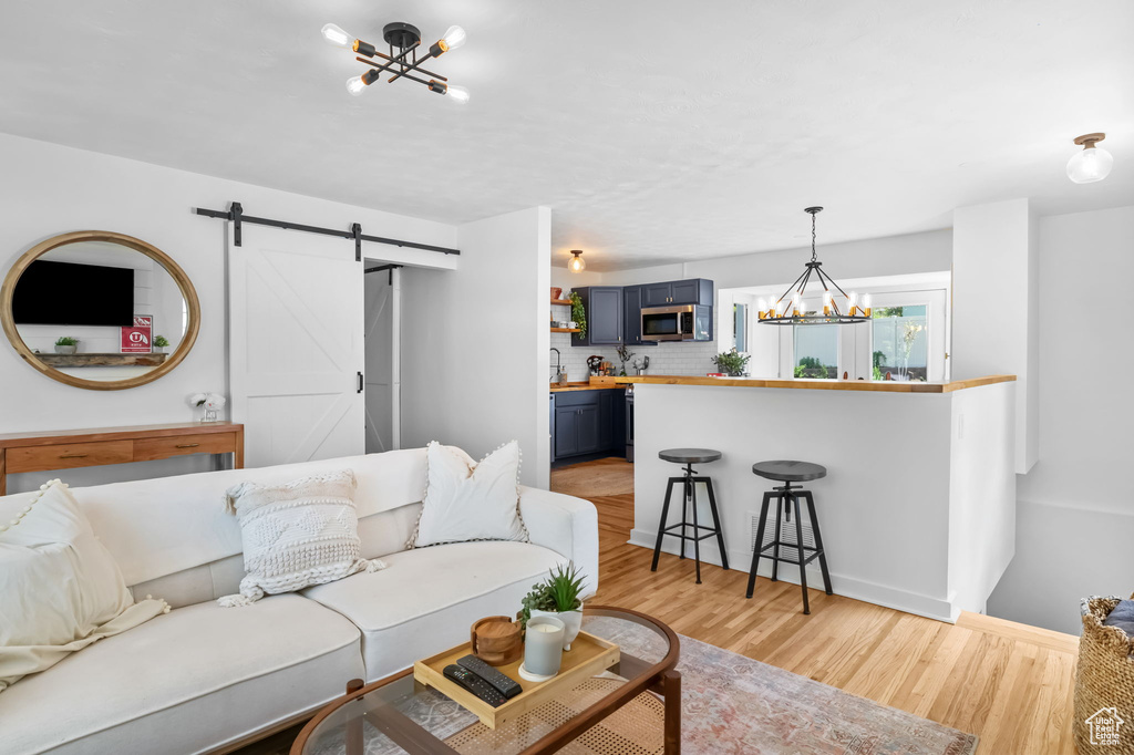Living room featuring a chandelier, a barn door, light wood-style flooring, and baseboards