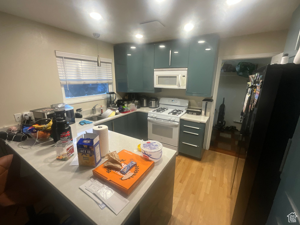 Kitchen featuring white appliances, a peninsula, light countertops, a sink, and light wood-style flooring