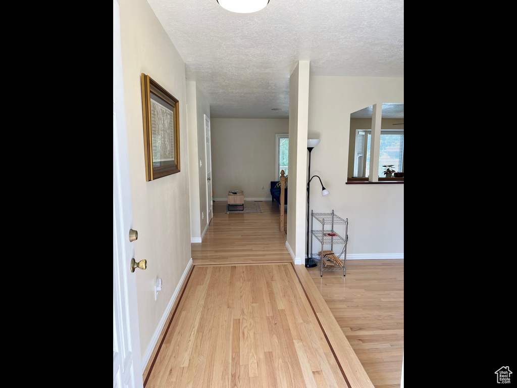 Corridor featuring a textured ceiling, light wood finished floors, and baseboards
