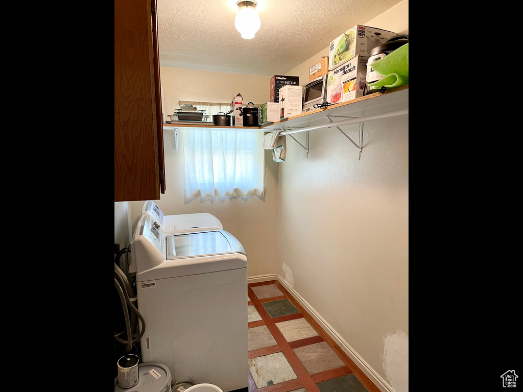 Clothes washing area featuring separate washer and dryer, a textured ceiling, and baseboards