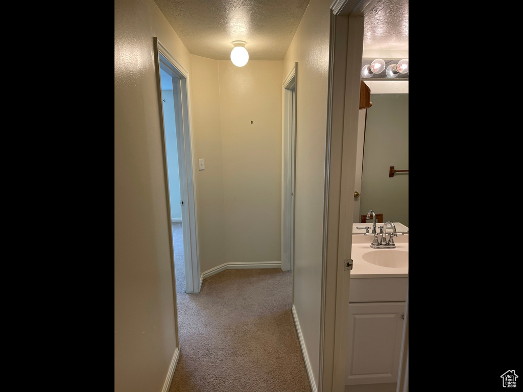 Corridor featuring a textured ceiling, carpet floors, baseboards, and a sink