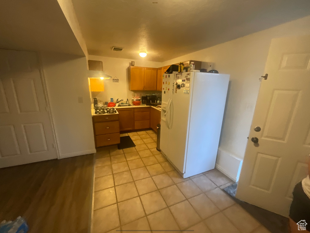 Kitchen with white fridge with ice dispenser, light tile patterned floors, light countertops, and a sink